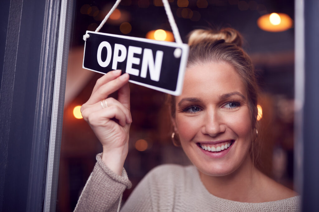 "A female business owner turning the 'Open' sign on the door of her small shop."